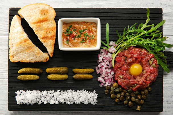 Steak tartar with chopped onio and pickles on a tray - Foto, Bild
