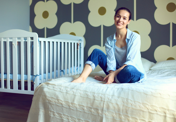 Young woman sitting on the bed near childrens cot. - Valokuva, kuva