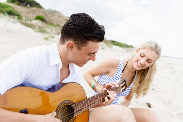 Young couple playing guitar on beach in love - Fotó, kép