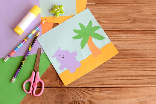 Paper hippo and palm tree applique, colored paper sheets, scissors, pencils, glue, eraser on wooden background with blank space for text. Funny children background. Art and craft project for kids  - Photo, Image