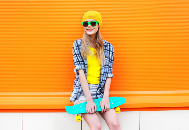 Fashion pretty blonde girl with skateboard in city over colorful - Фото, изображение
