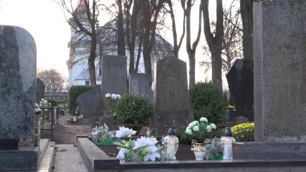Kaarsen branden tussen grafstenen in begraafplaats en kerk in kleine stad. 4k - Video