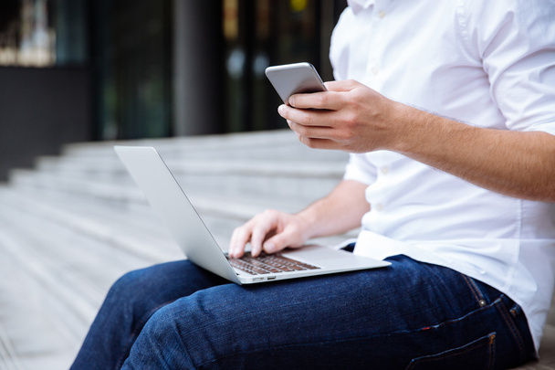 Closeup of young businessman using laptop and cell phone outdoors - Photo, Image