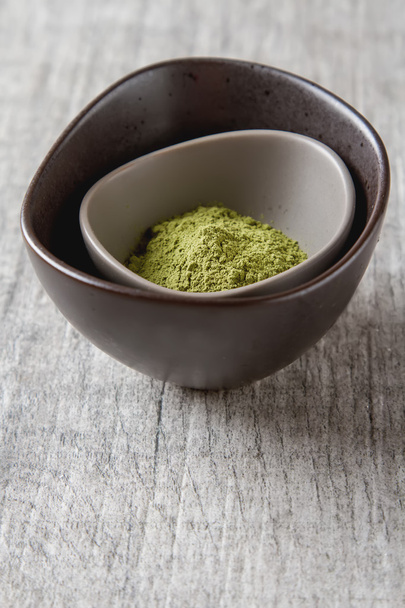Dry Matcha tea in a small brown plate. Grey wood background - Φωτογραφία, εικόνα