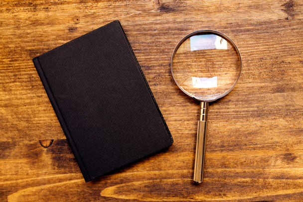 Loupe magnifying glass and notebook on wooden desk, top view - 写真・画像