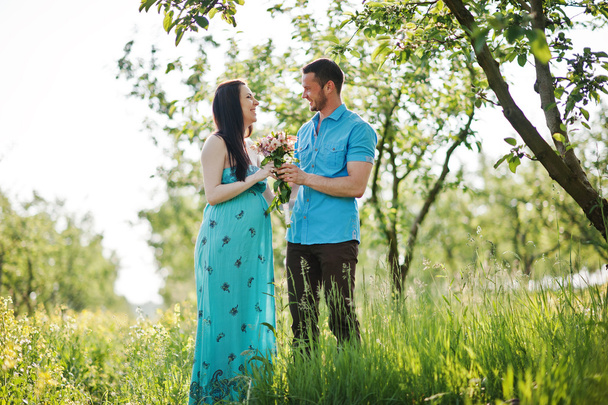 Happy pregnant couple at turquoise dress on the garden - Photo, Image