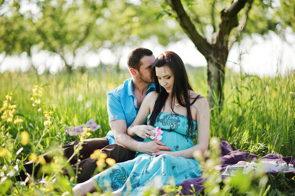 Happy pregnant couple at turquoise dress on the garden - Foto, Imagem