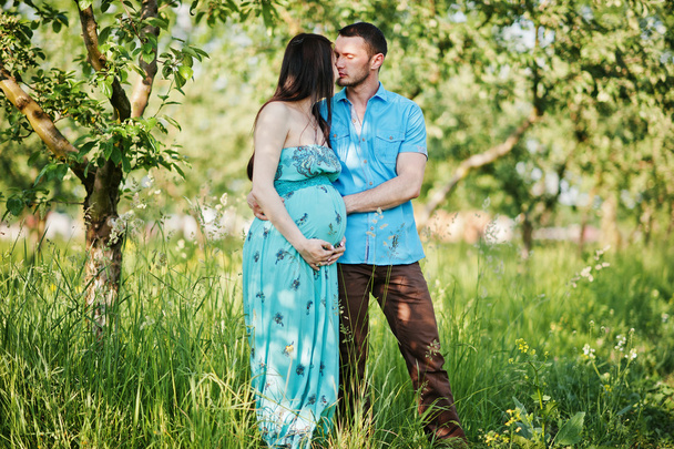 Happy pregnant couple at turquoise dress on the garden - Fotoğraf, Görsel