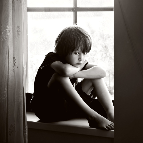 Sad child, boy, sitting on a window shield - 写真・画像