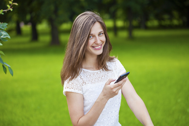 Woman texting on the smart phone walking in the summer park - Foto, imagen
