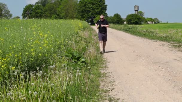 Muž běží podél okraje venkovské silnice v létě - Záběry, video