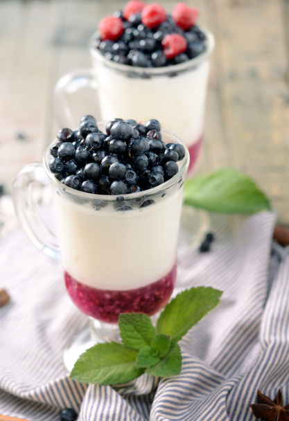 Delicious parfait dessert with bilberry, milk souffle and jello layers. Frozen treat in a glass on rustic wooden background - Foto, Imagen
