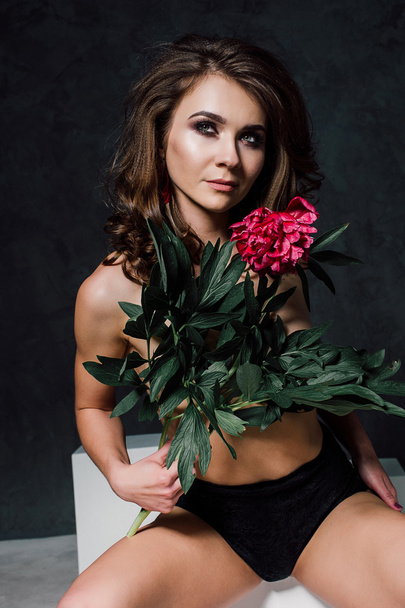 Beautiful sexy stylish young adult in lingerie with nice bouquet of pink peonies. Studio retouched shot. - Fotó, kép