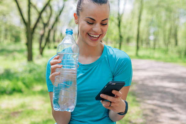 Girl is drinking water after treaning and using mobile phone - Foto, imagen