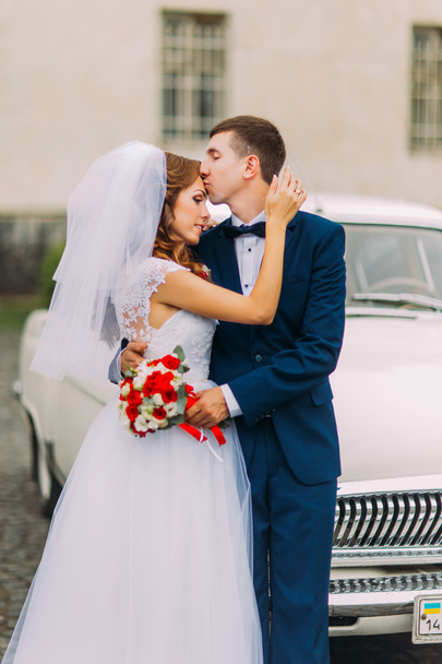 Happy just married couple holding each other in the background of vintage car - Fotoğraf, Görsel
