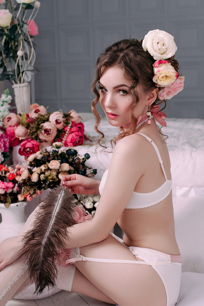 部屋の白いランジェリーを着て、美しい若いセクシーな女性は、花で飾られました。完璧なメイク。美容ファッション。まつげ。レタッチ スタジオ撮影.  - 写真・画像