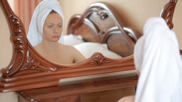 Woman applying mask moisturizing skin cream on face looking in mirror. - Filmati, video