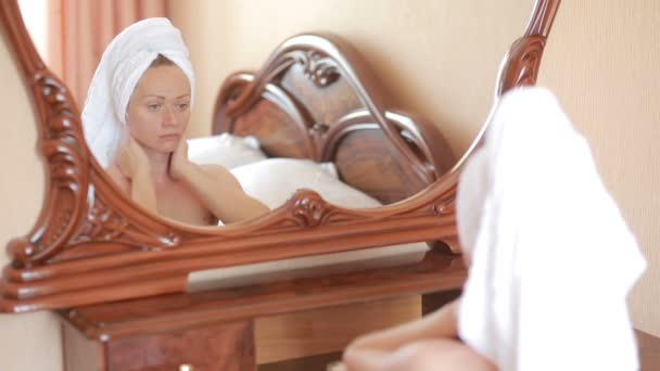 Mujer aplicando mascarilla hidratante crema para la piel en la cara mirando en el espejo
. - Imágenes, Vídeo