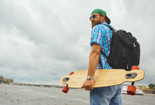 Handsome hipster guy stand with longboard over city river background. - Foto, Imagem