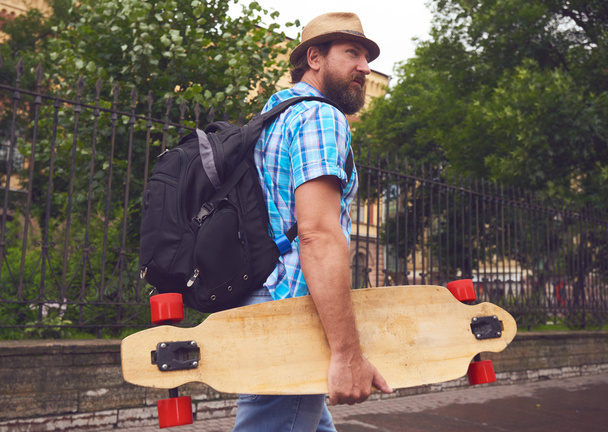 Freaky bearded man walking with longboard - Foto, imagen