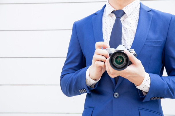 Stylish man in blue suit holding vintage camera in white vintage fence background. - Foto, afbeelding