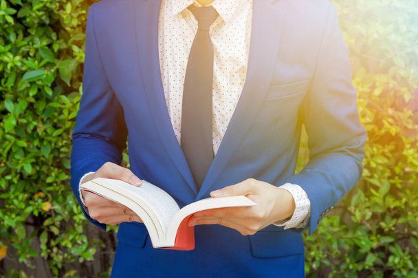 Young businessman reading book in green nature background - Photo, image