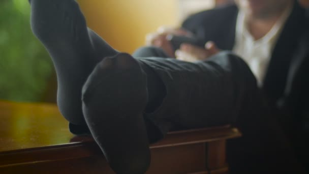 Расслабленный босс ставит ноги на стол во время работы над мобильным телефоном
 - Кадры, видео