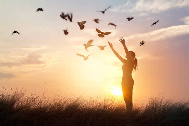 Donna che prega tra uccelli liberi godendo la natura sullo sfondo del tramonto
 - Foto, immagini
