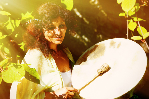 beautiful shamanic girl playing on shaman frame drum in the nature. solar light effect. - Photo, Image