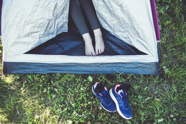 Frauenbeine im offenen Zelt und Turnschuhe im Gras. - Foto, Bild