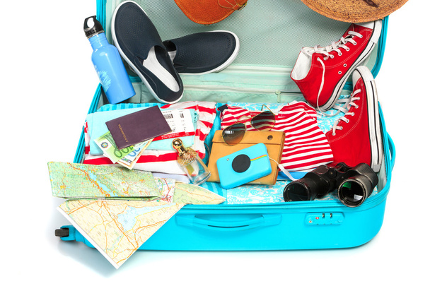 The open blue suitcase, sneakers, clothing, hat, and retro camera on white background. - Photo, Image
