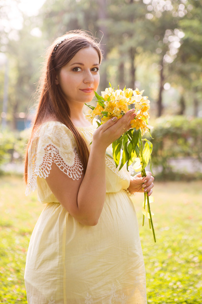 the young beautiful pregnant woman with flowers in park in summer day - Foto, imagen