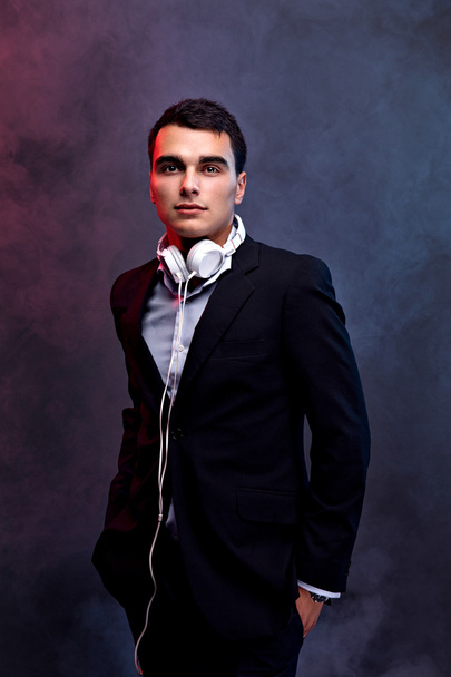 Portrait of a fashion guy listening music with headphones. Studio shot. Dark background. - Foto, afbeelding