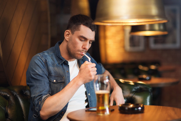 man drinking beer and smoking cigarette at bar - Photo, image