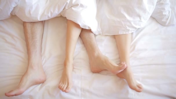a man and a woman in bed. male and female legs top view, white linens - Video