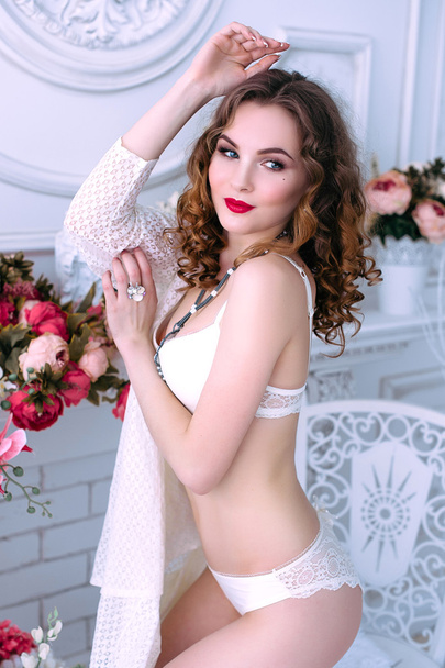 Όμορφη νεαρή σέξι γυναίκα, φορώντας λευκά εσώρουχα, αίθουσα διακοσμημένη με λουλούδια. Τέλειο μακιγιάζ. Ομορφιά μόδα. Βλεφαρίδες. Studio retouched βολή.  - Φωτογραφία, εικόνα
