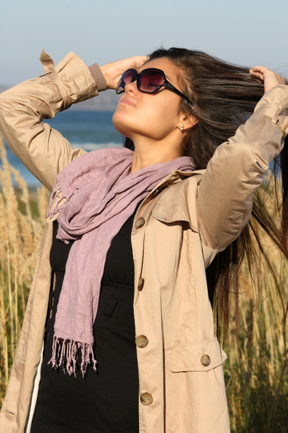 Дівчина в бежевому осінньому пальто, що виправляє волосся
 - Фото, зображення