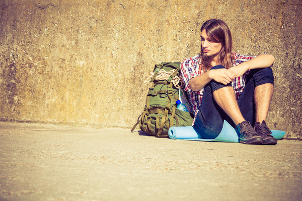 Man tourist backpacker sitting by grunge wall outdoor - Zdjęcie, obraz