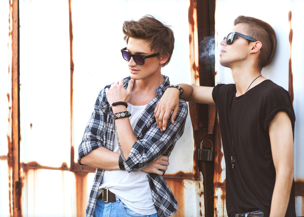 Two fashion guy smoking, are posing near Iron begraunda - Photo, image