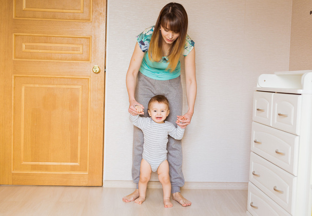 Madre enseñando a su lindo hijo pequeño a caminar cogido de la mano cuerpo parte primer bebé pasos concepto
 - Foto, Imagen
