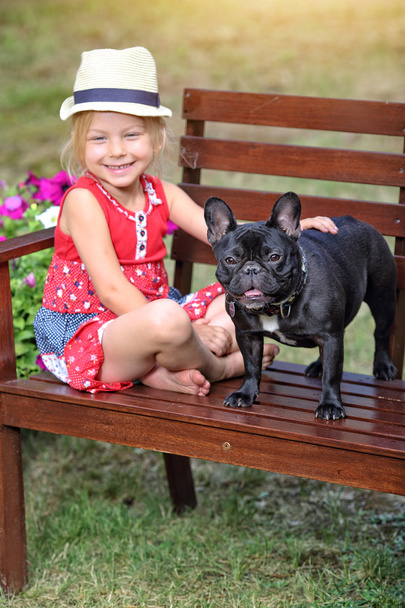 girl in a hat sitting on a bench with a dog - Foto, imagen