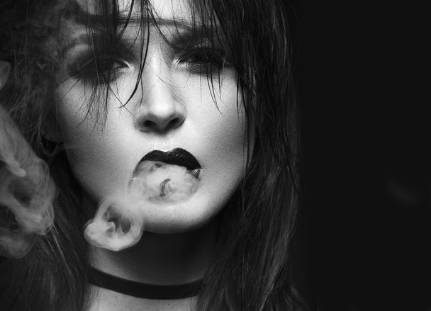 Beautiful sexy brunette girl with bright makeup, red lips, smoke from mouth. beauty face. Black and white - Фото, изображение