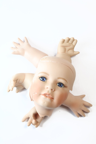 Rikkoutunut nuken pää ja ruumiinosat valkoisella taustalla
 - Valokuva, kuva