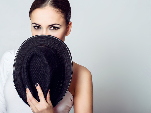 Jeune fille brune cachant son visage derrière un chapeau noir
. - Photo, image