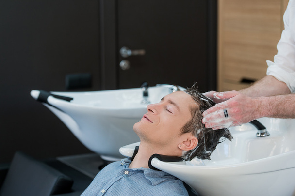 Close-up de um jovem tendo seu cabelo lavado no salão de cabeleireiro
 - Foto, Imagem