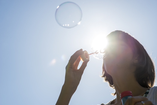 Mujer soplando burbujas bajo la luz del sol brillante
 - Foto, imagen
