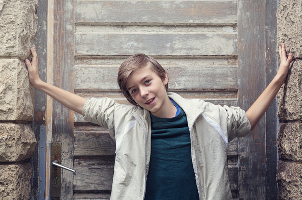 retrato de um menino sorridente em pé na frente de uma entrada antiga
 - Foto, Imagem