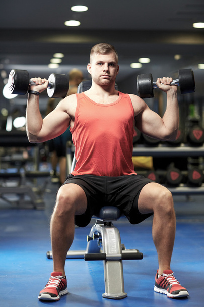 young man with dumbbells flexing muscles in gym - Foto, afbeelding