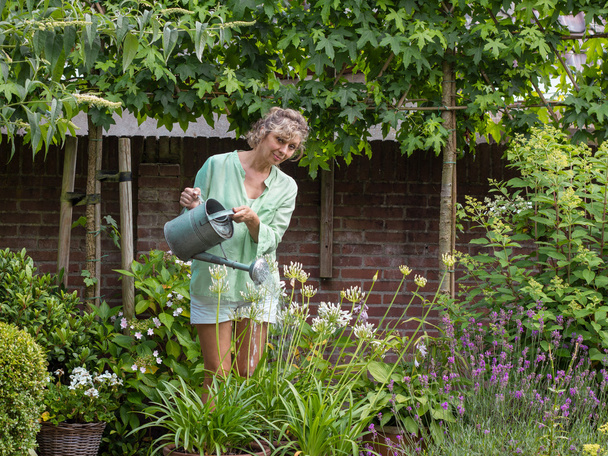 Blonďatá žena středního věku zalévat květiny v zahradě - Fotografie, Obrázek