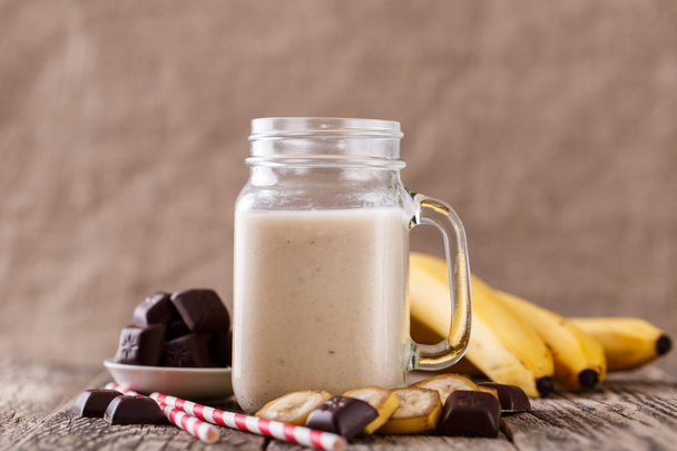 Batido de plátano con chocolate en frasco de vidrio con paja para beber
 - Foto, imagen